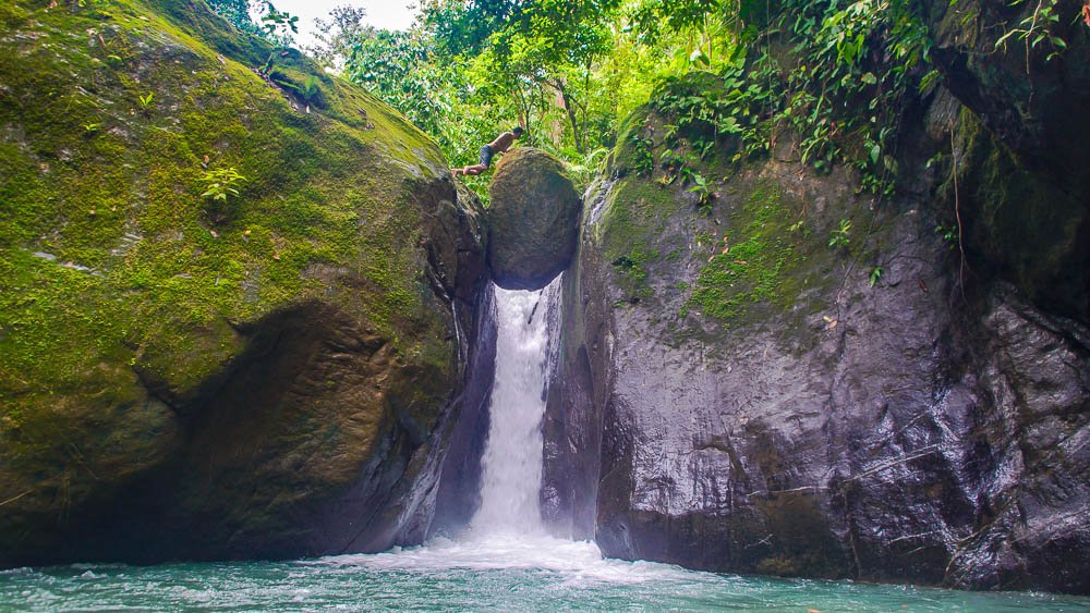 man standing on balanced rock of pavon waterfall tour manuel antonio
 - Costa Rica
