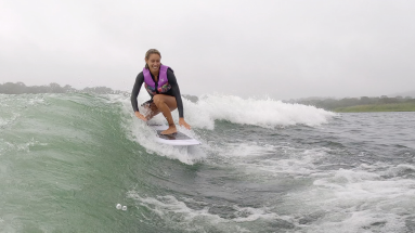 a smiling lady wakesurfs on lake arenal trying to keep balance
 - Costa Rica